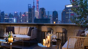A rooftop terrace with a city skyline view, furnished with a sofa, chairs, and a table with champagne and candles. - Elegant International Hotel Shanghai - Bund Sichuan Road North Metro Station Branch (Shanghai)