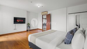 Un dormitorio moderno con una cama grande, un televisor montado en la pared y suelo de madera.