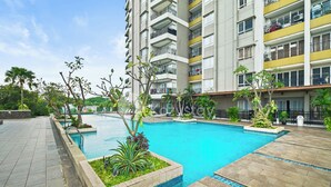 Un moderno edificio residencial con piscina, rodeado de vegetación y un camino empedrado.