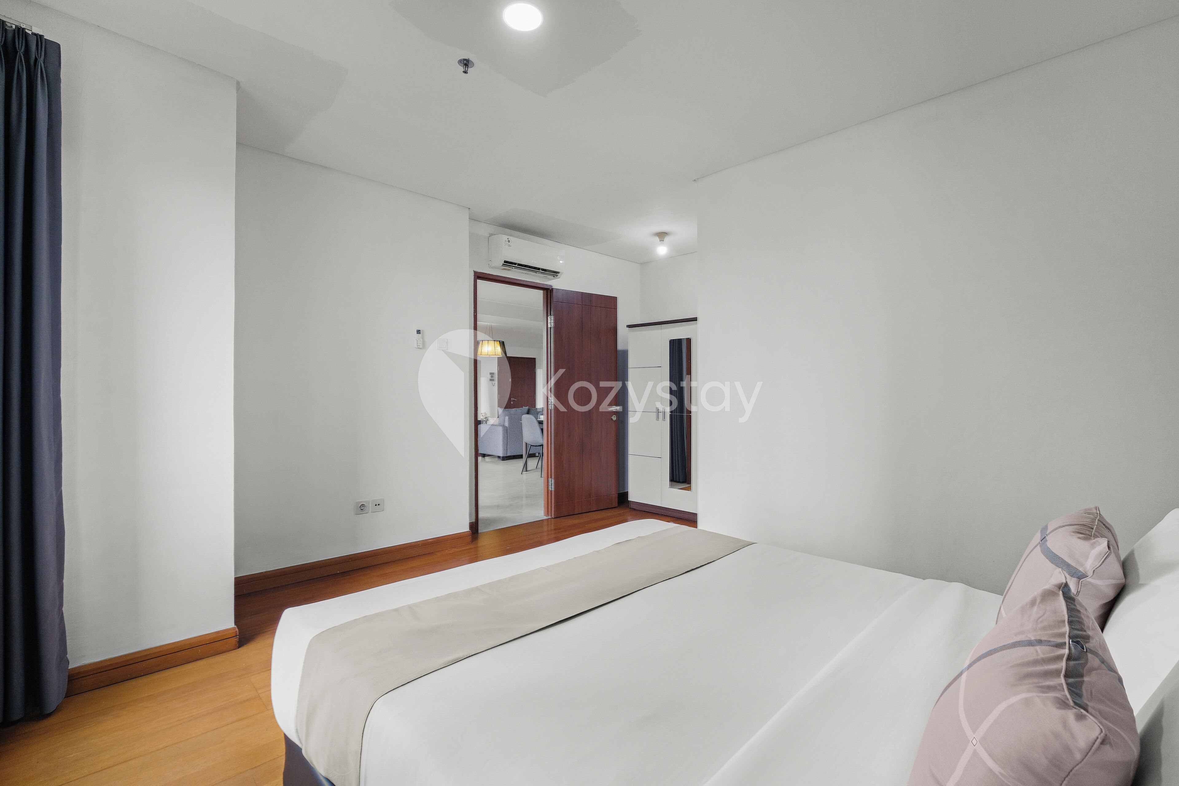 Una habitació d'hotel moderna amb un llit gran, un paviment de fusta, parets blanques i un aparell d'aire condicionat.