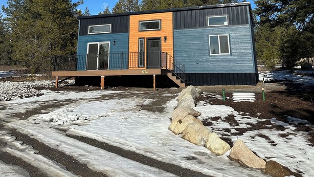 A modern two-story cabin with a wooden deck and a black staircase. - Modern Tiny House in the Woods (Athol)