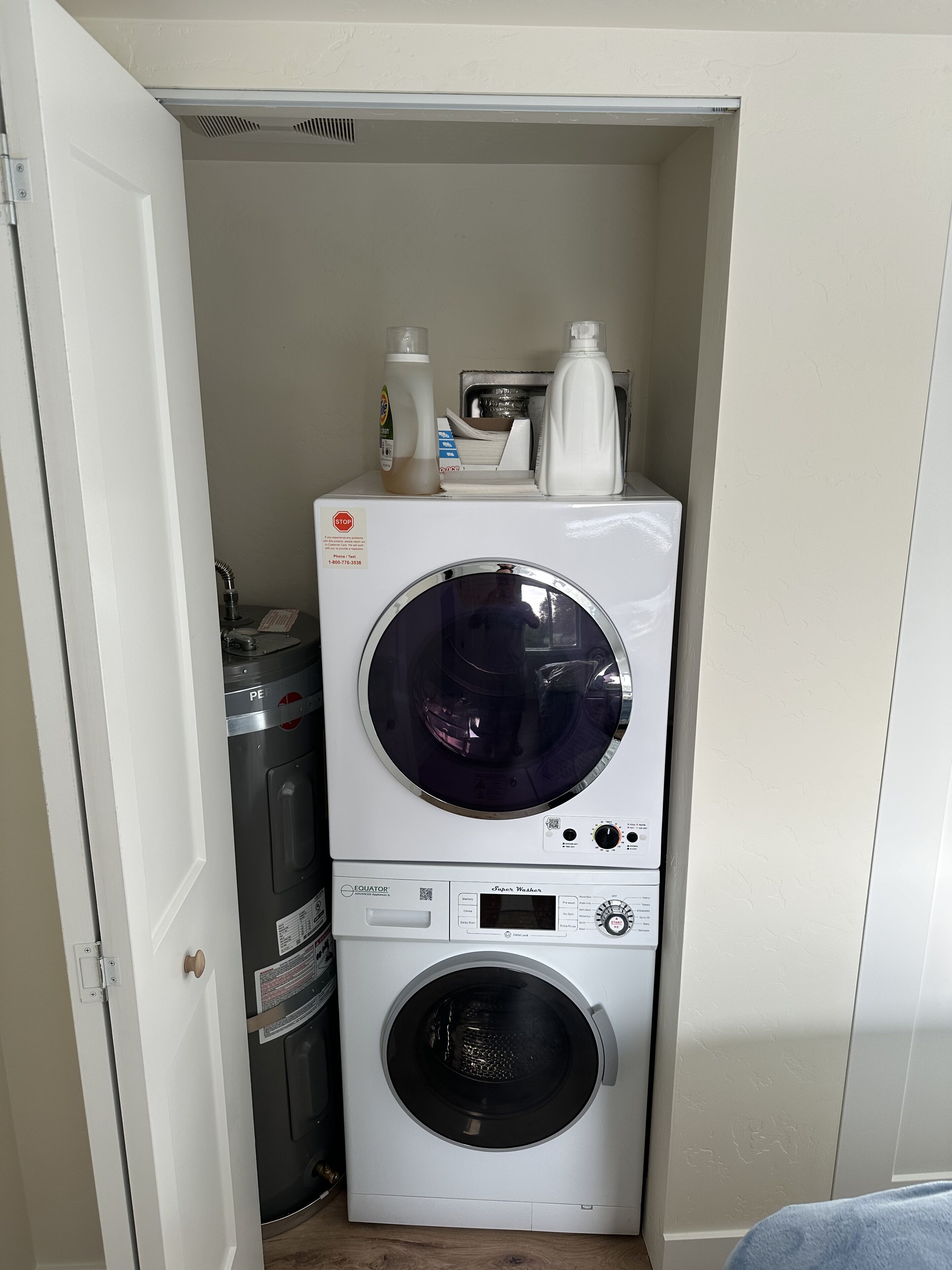 Een kleine wasruimte met een voorlader wasmachine en droger, verticaal boven elkaar geplaatst.