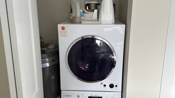 Een kleine wasruimte met een voorlader wasmachine en droger, verticaal boven elkaar geplaatst.