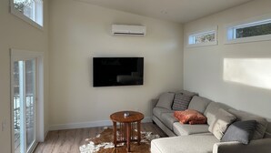 A living room with a grey sofa, a mounted TV, a wooden side table, and a cowhide rug. - Modern Tiny House in the Woods (Athol)