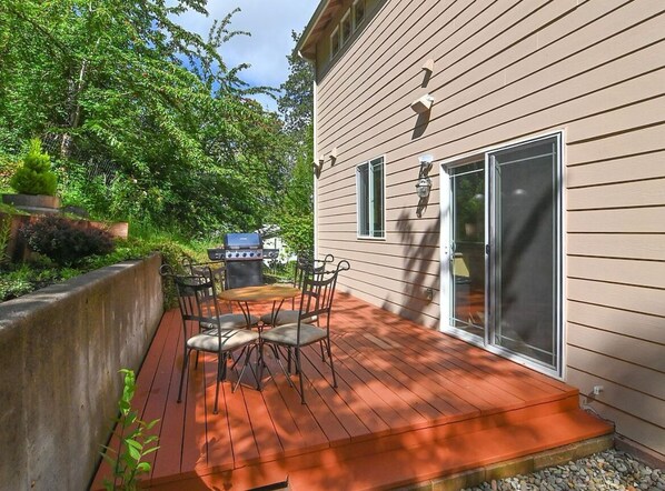 Une terrasse avec un barbecue et des chaises, une porte-fenêtre coulissante et une maison au revêtement de couleur beige.