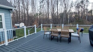 A deck with a table and chairs, a covered grill, and a house in the background.