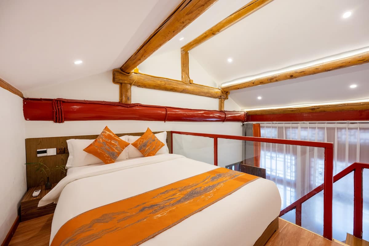 A hotel room with a large bed, wooden beams, a red railing, and a view of the outside.