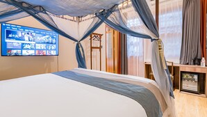 Ein Schlafzimmer mit einem Bett, einem an der Wand montierten Fernseher, der verschiedene Bilder zeigt, und einem kleinen Kühlschrank.