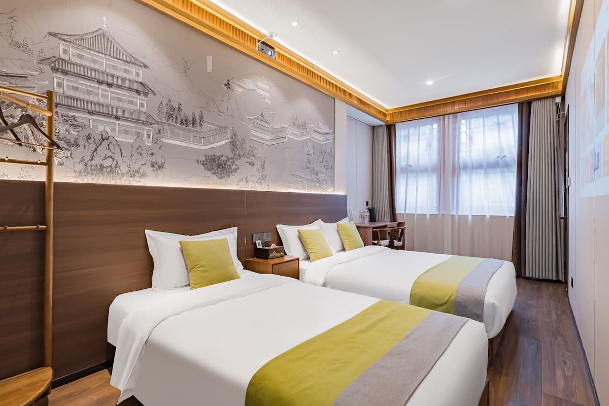 A hotel room with two beds, a wooden headboard, a mural, and a desk with a chair.