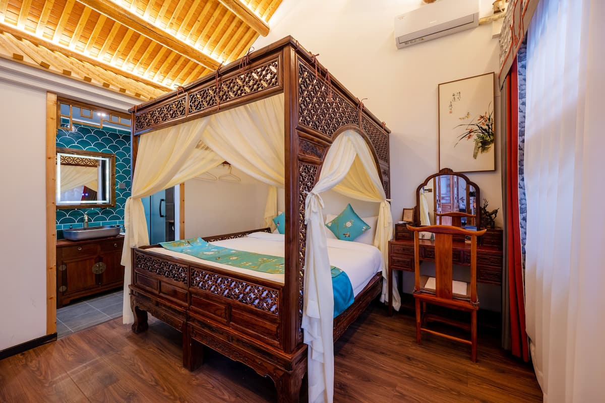 A four-poster bed with a canopy, a wooden nightstand, a mirror, and a wall-mounted air conditioner.