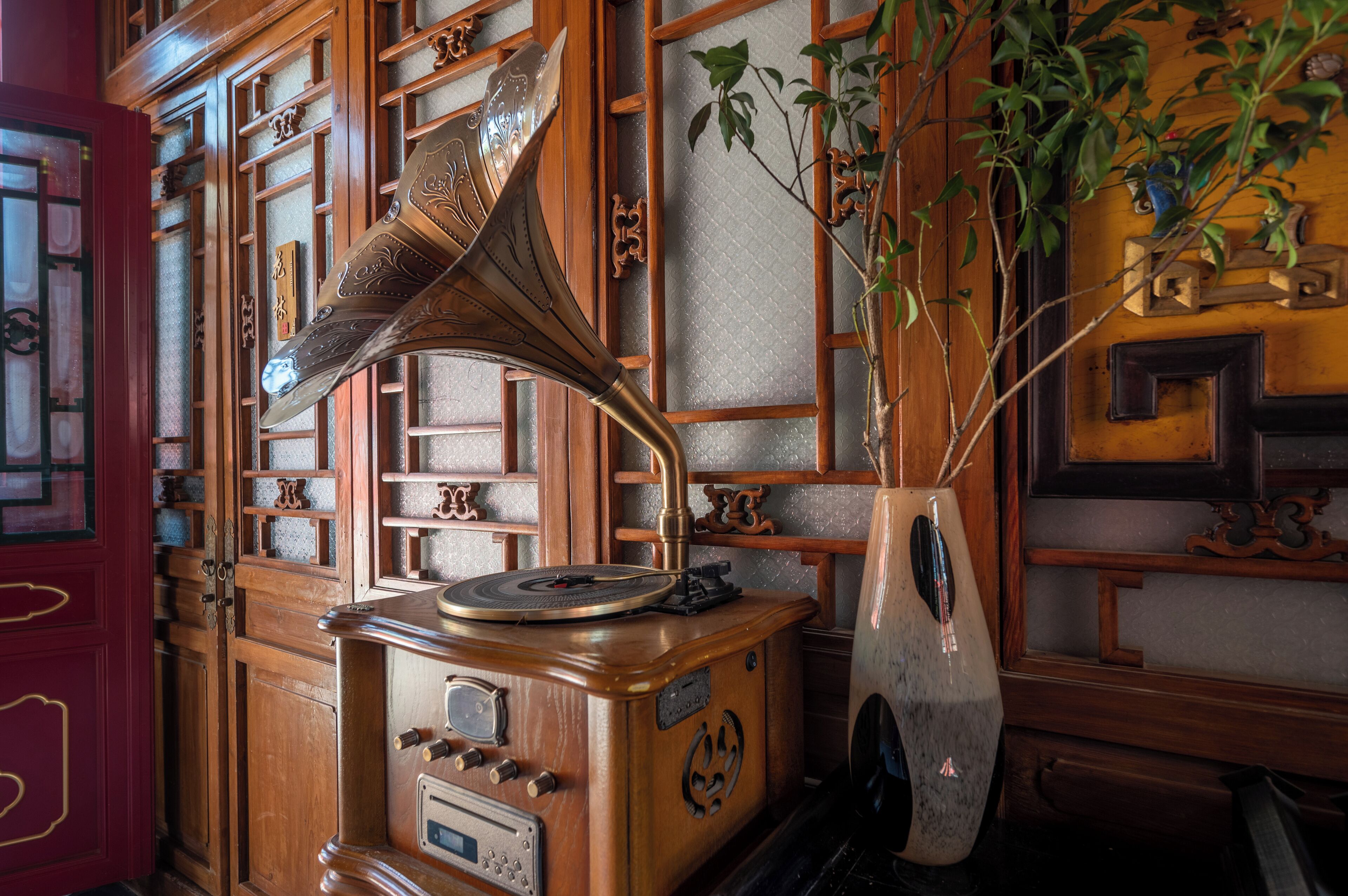 Un gramófono antiguo con un cuerno, sobre un mueble de madera con diseños intrincados y una planta a su lado.