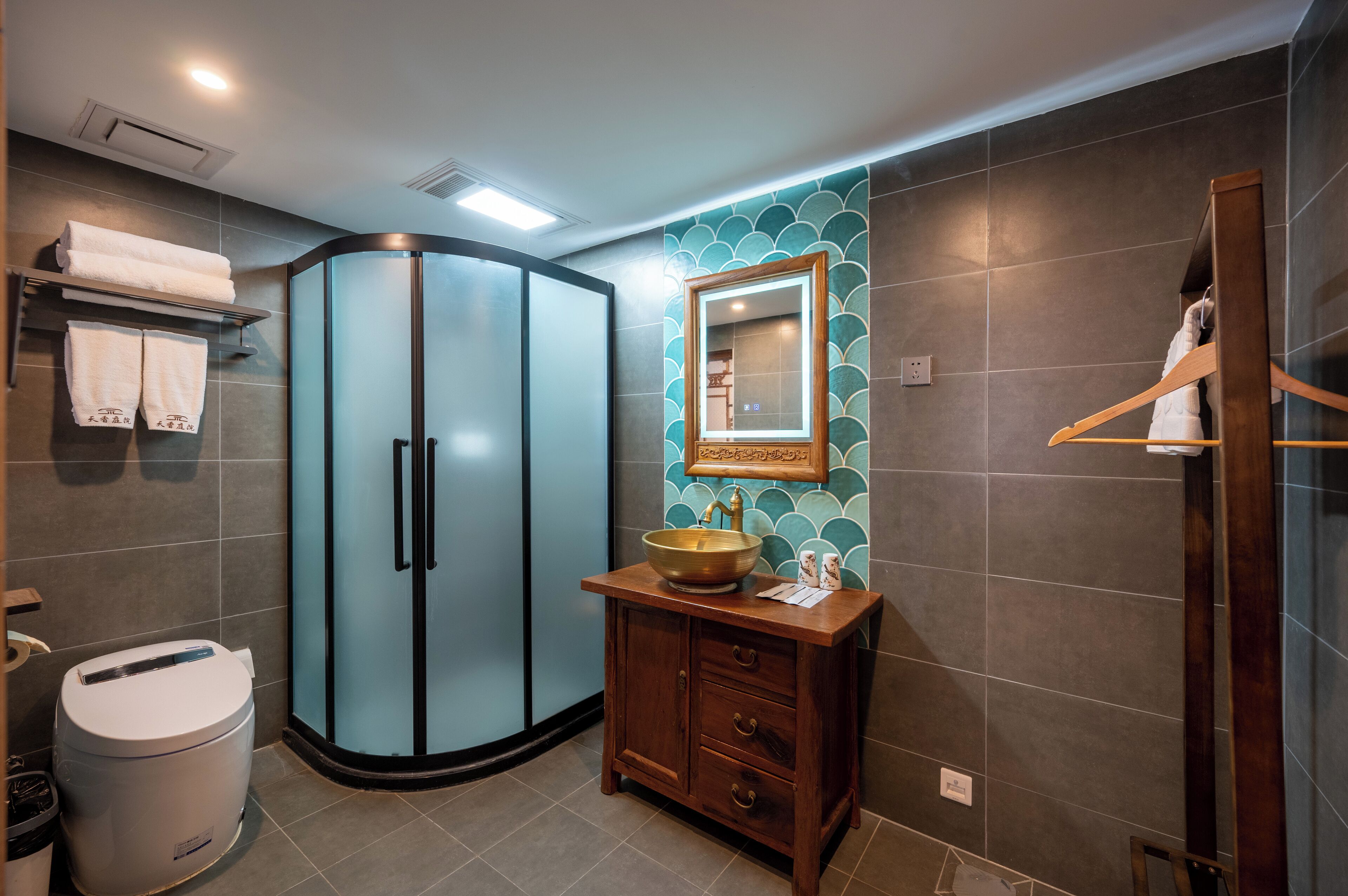 Une salle de bain dotée d’une douche à parois courbes en verre, d’un meuble-lavabo en bois avec un vasque et d’un miroir orné d’un cadre décoratif.