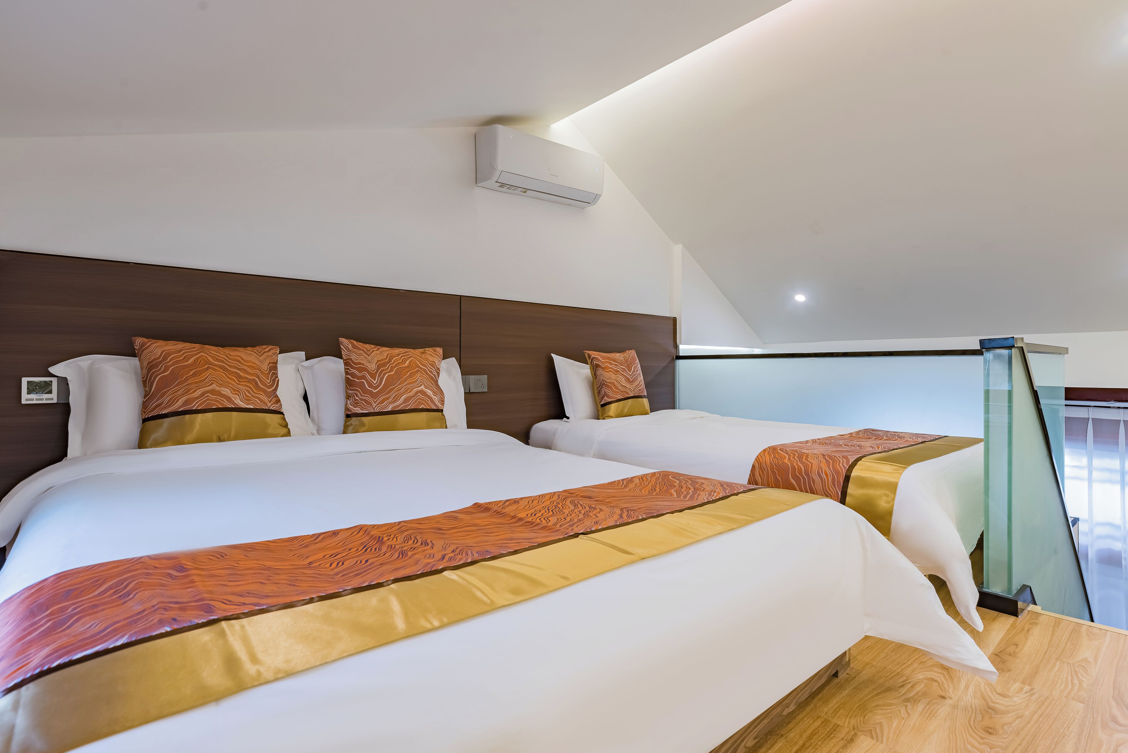 Une chambre d’hôtel avec deux lits, chacun doté d’une tête de lit en bois, de draps blancs et de coussins décoratifs à motifs orange. Un appareil de climatisation est fixé au plafond.