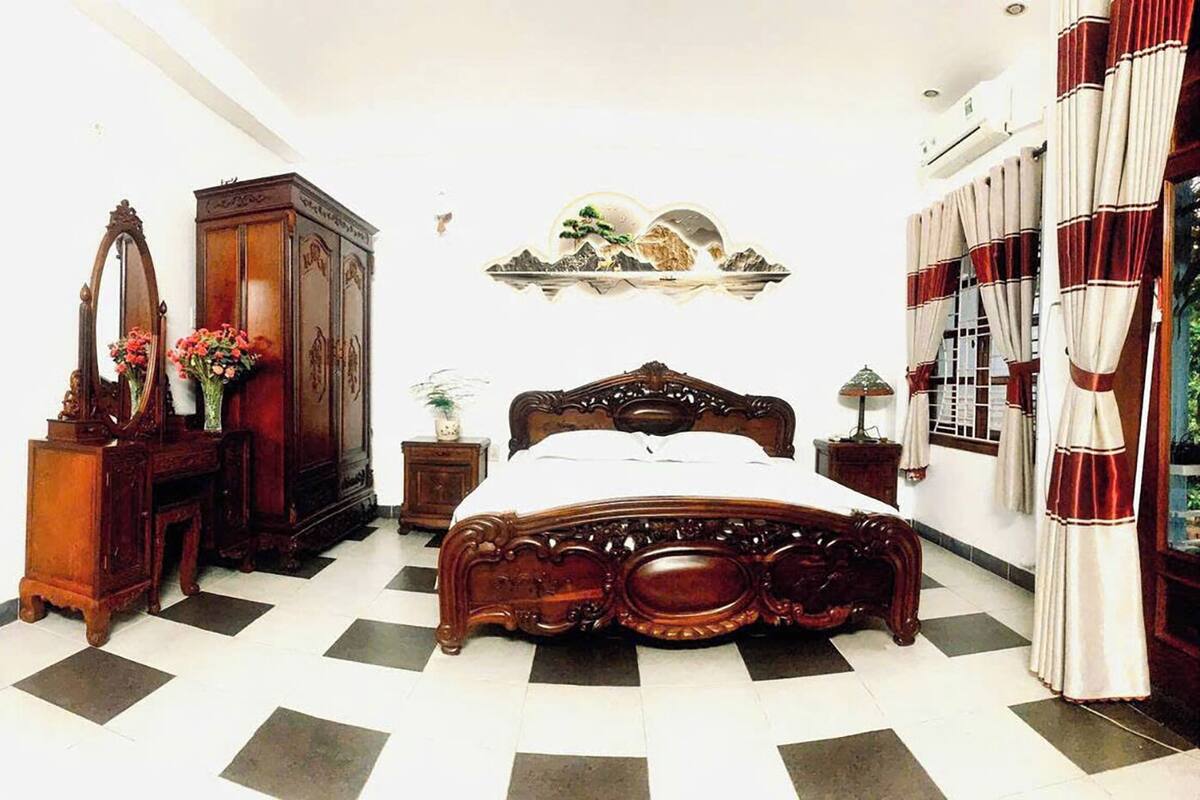 A bedroom with a checkered floor, a wooden bed, a dresser, a mirror, and a shelf with decorative items.