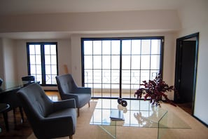 Relax in this stylish living space, featuring a glass coffee table, comfortable armchairs, and a large window with a grid pattern.