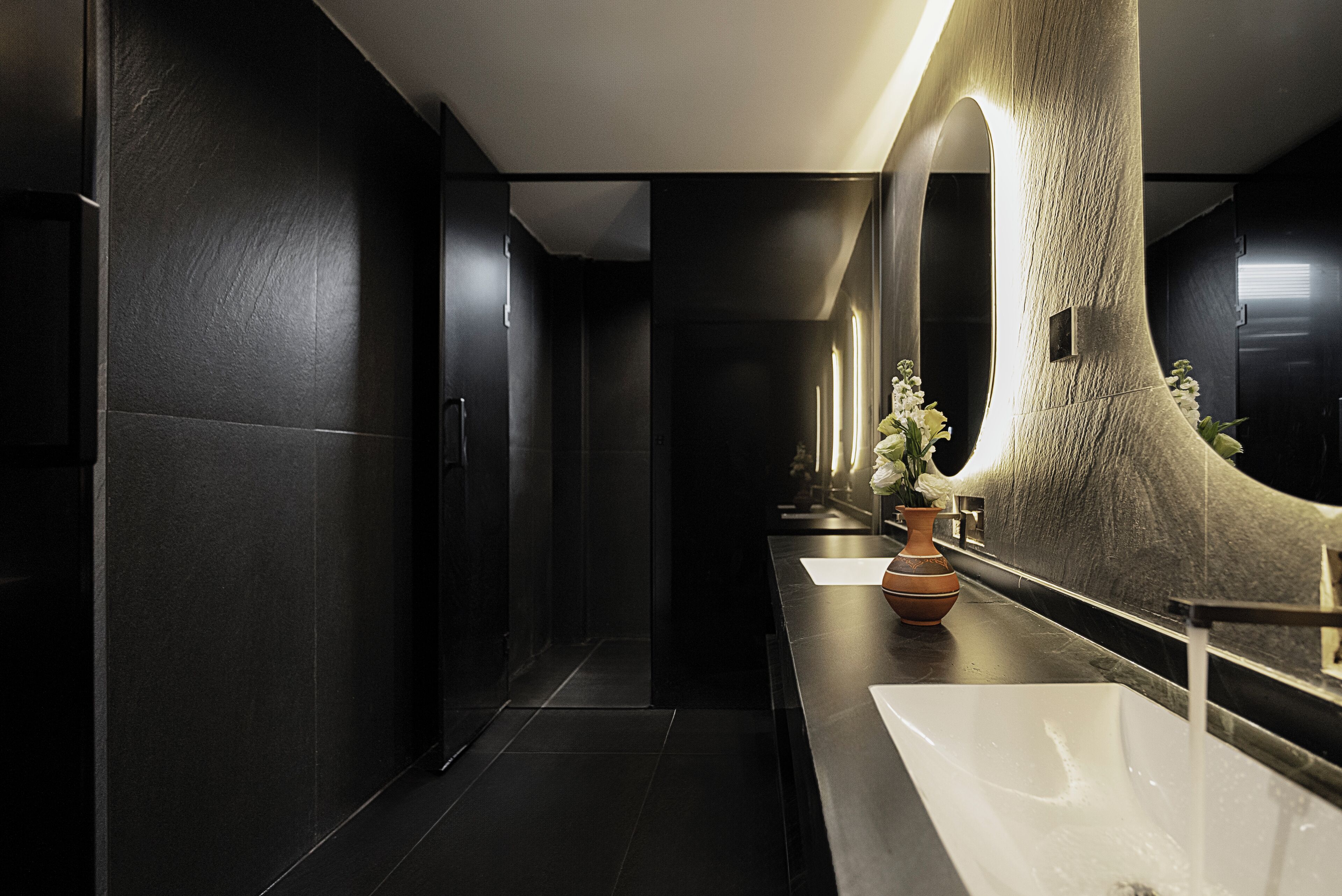 A modern bathroom with a large mirror, a white sink, and a vase with flowers.