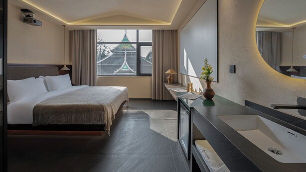 A modern hotel room with a large bed, a bathroom with a large mirror and sink, and a view of a traditional building outside the window. - Jinghong Chen Duo Nan Shan Man Zhen (Xishuangbanna Dai)