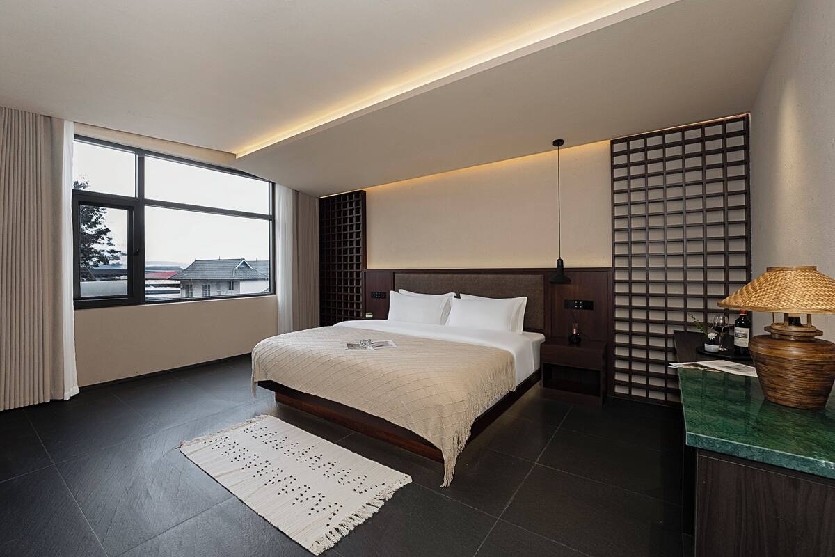 Ein modernes Schlafzimmer mit einem großen Bett, Blick ins Freie, einem Holzkopfstück und einem Nachttisch mit einer Lampe.