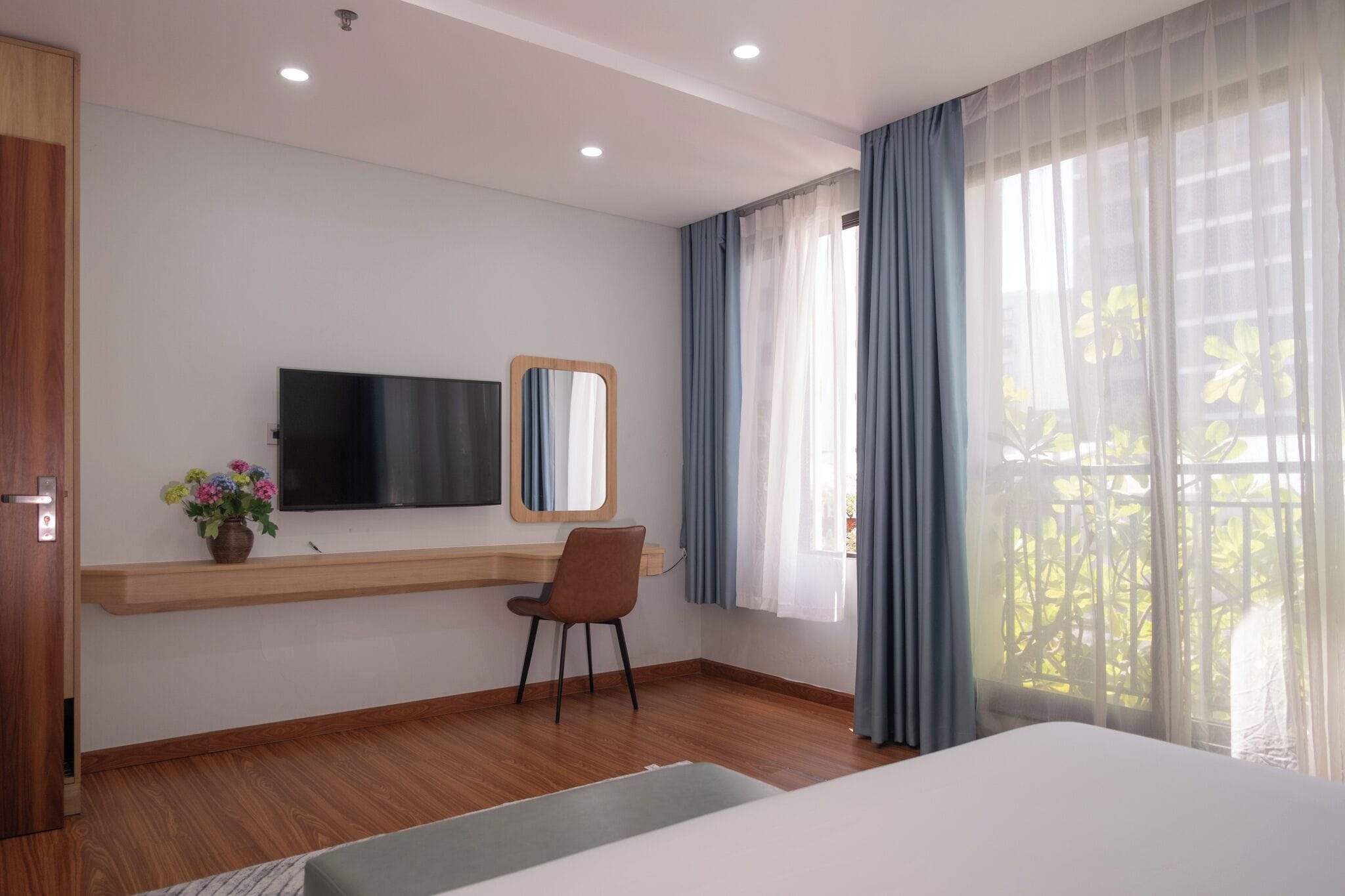Habitación de hotel con cama, escritorio con silla, televisor, espejo y ventana con cortinas.