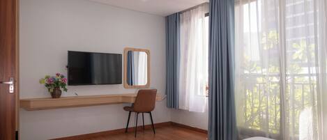 Habitación de hotel con cama, escritorio con silla, televisor, espejo y ventana con cortinas.