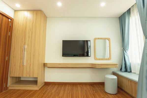 A modern bedroom with a wooden wardrobe, a mounted TV, a mirror, and a bench by the window.