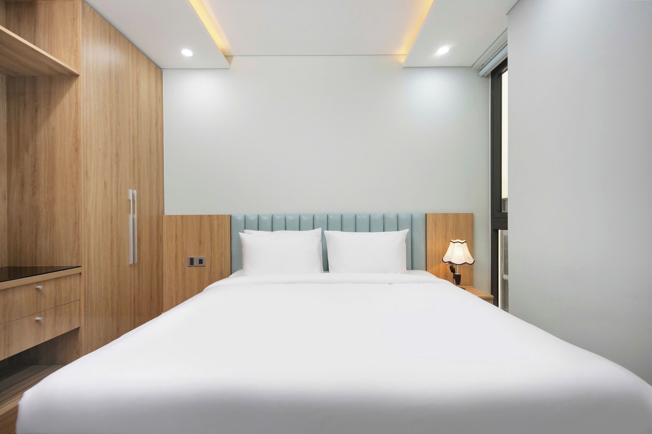 A modern hotel room with a large bed, wooden wardrobe, and a nightstand with a lamp.