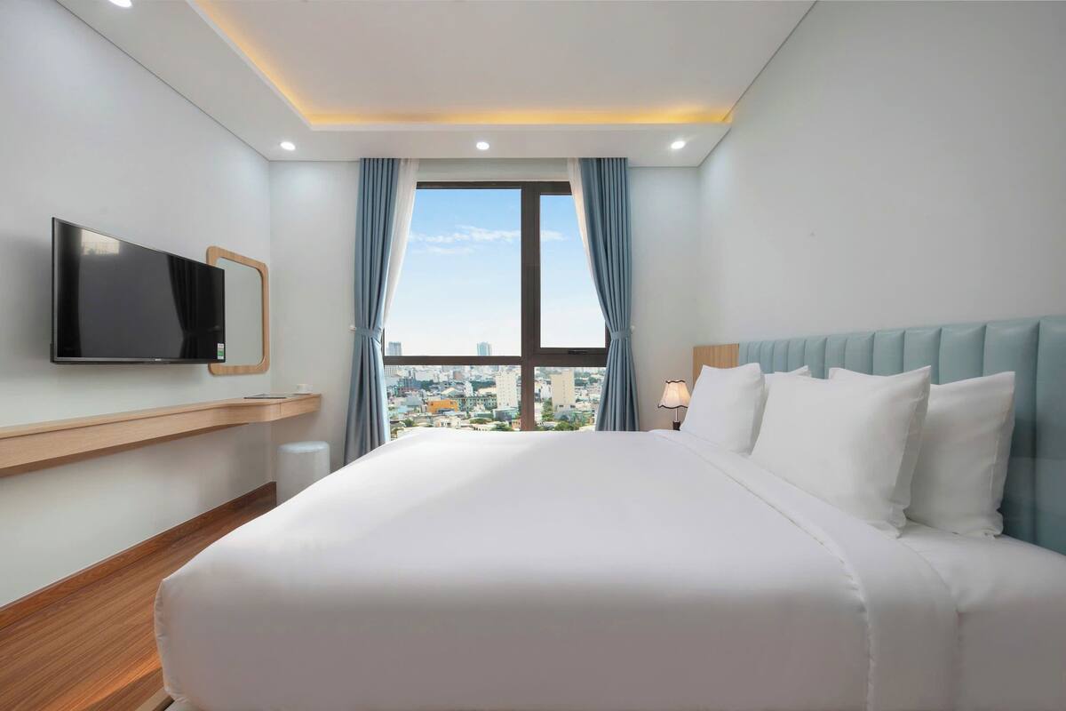 Ein Hotelzimmer mit einem großen Bett, einem an der Wand montierten Fernseher und Blick auf die Stadt durch das Fenster.