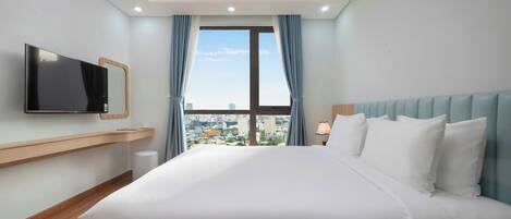 Une chambre d’hôtel avec un grand lit, un téléviseur fixé au mur et une vue sur la ville par la fenêtre.
