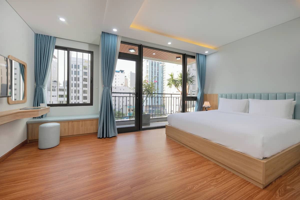 Ein modernes Hotelzimmer mit einem großen Bett, einer Bank, einem kleinen Hocker, einem Spiegel und einem Fenster mit Vorhängen.