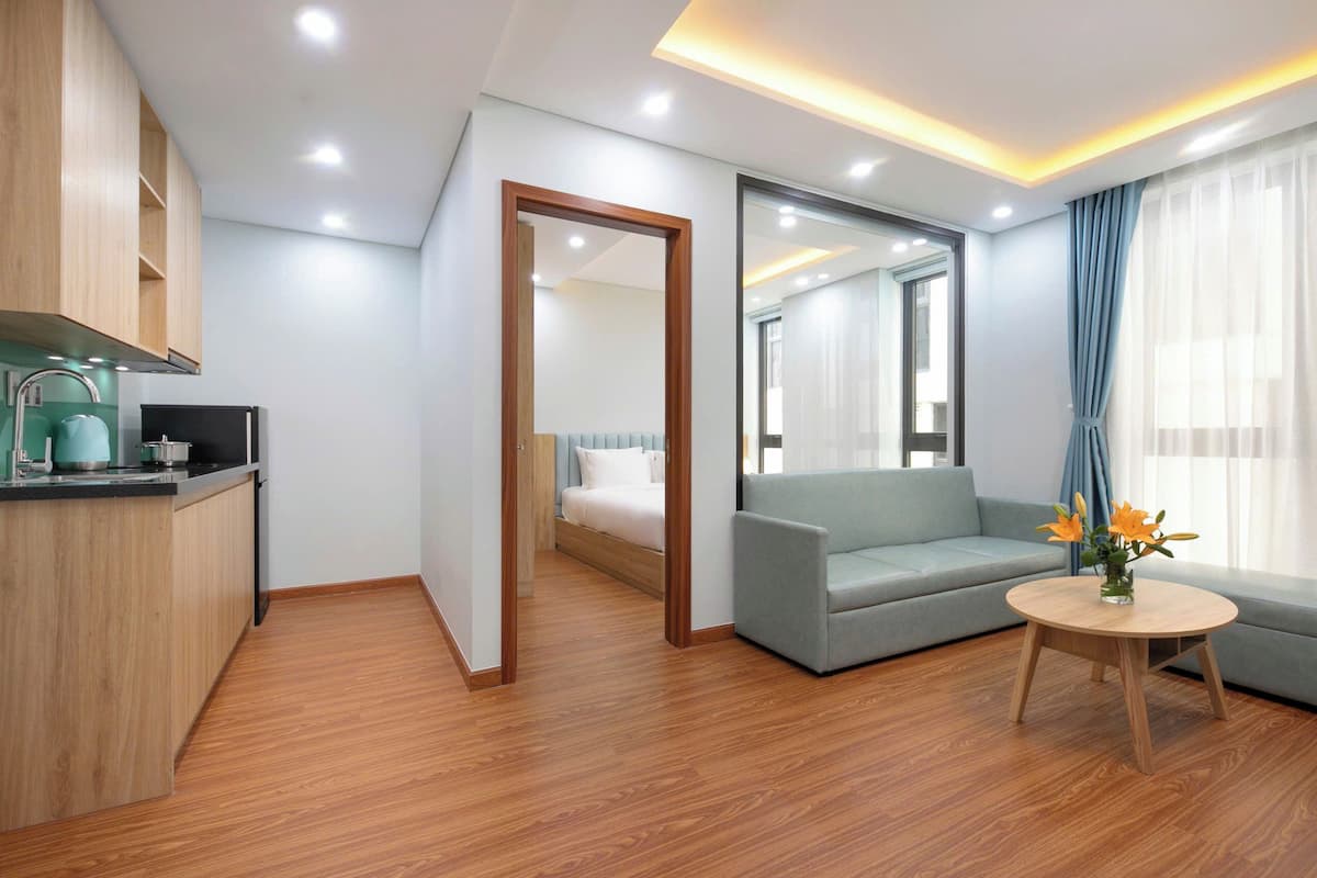 Ein modernes Hotelzimmer mit Küchenzeile, einer Couch, einem runden Holztisch und einem Spiegel.
