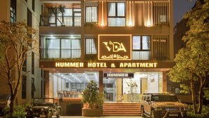 Ein mehrstöckiges Gebäude mit Balkonen, einem Schild mit der Aufschrift "HUMMER HOTEL & APARTMENT" und einem vor der Fassade stehenden Hummer SUV.