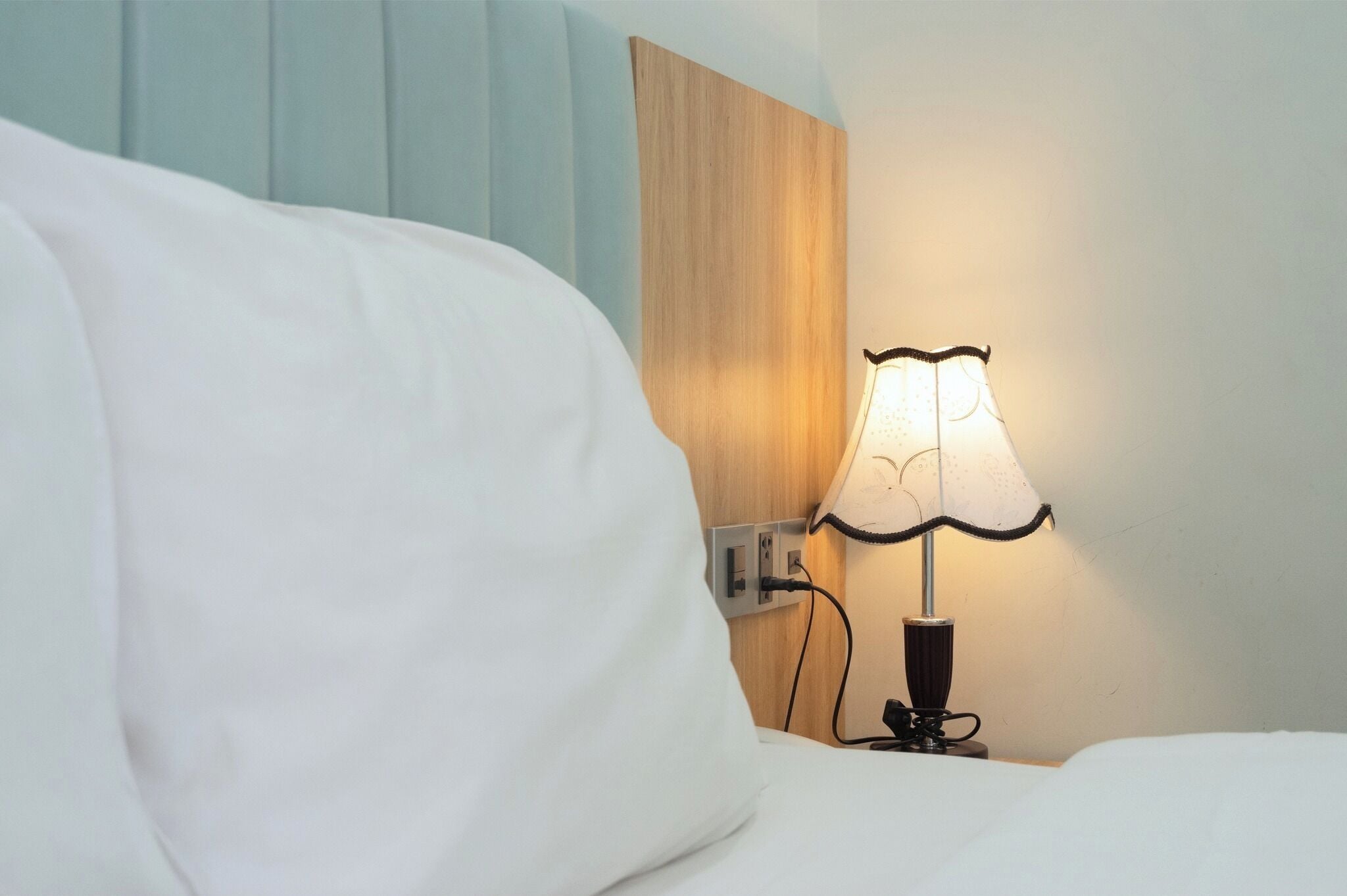 A bed with white sheets, a bedside lamp, and a wooden headboard.