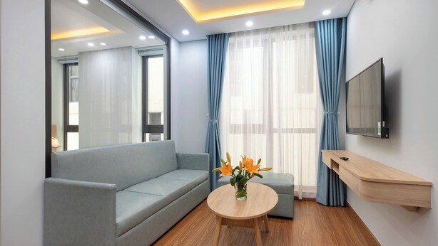 Ein modernes Wohnzimmer mit einem grauen Sofa, einem runden Couchtisch mit Blumenvase und einem an der Wand befestigten Fernseher.
