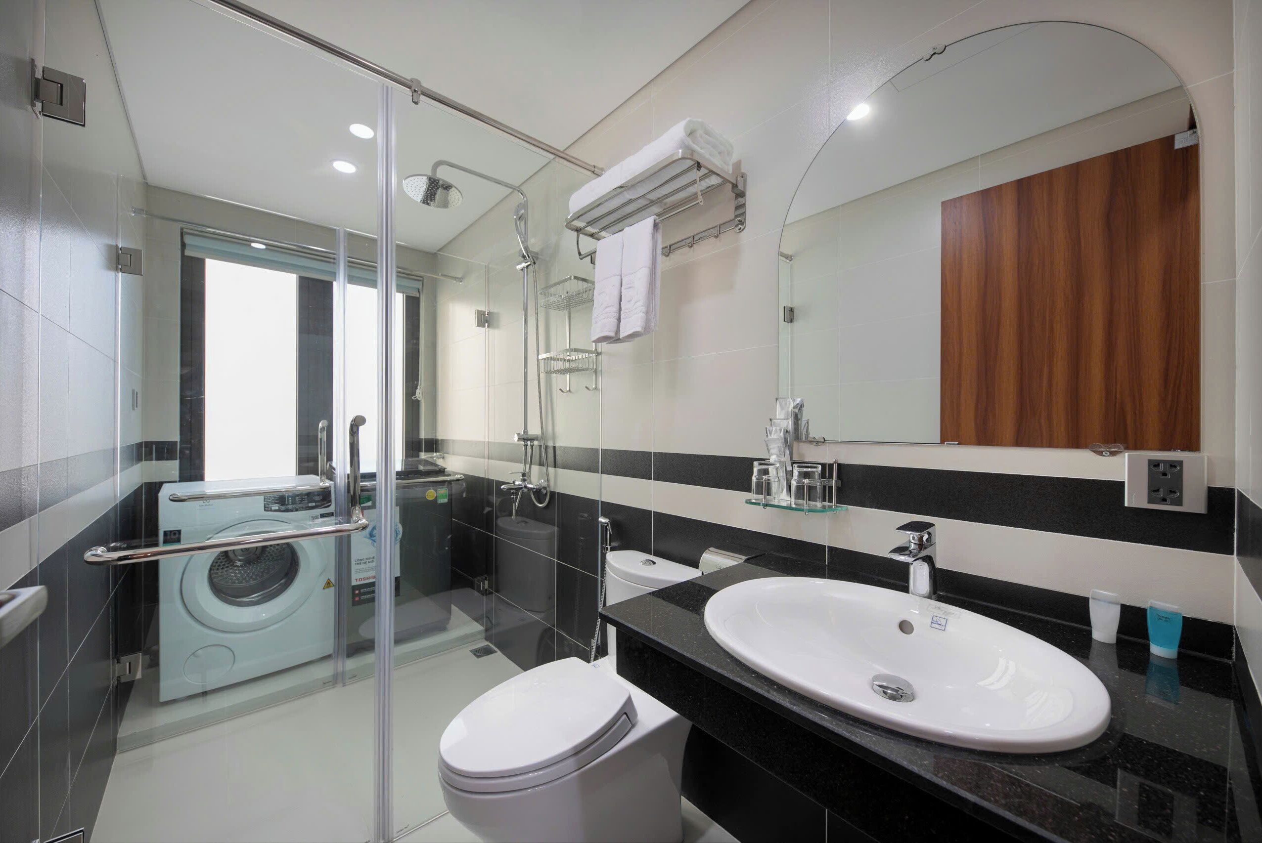 Ein modernes Badezimmer mit Glasdusche, Waschmaschine, Toilette und Waschbecken mit Spiegel darüber.