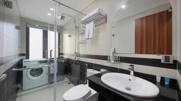 Ein modernes Badezimmer mit Glasdusche, Waschmaschine, Toilette und Waschbecken mit Spiegel darüber.