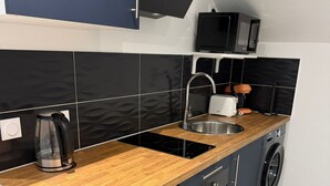 A modern kitchen with a wooden countertop, stainless steel sink, and a built-in oven. - Charming studio near Roissy CDG (Vaujours)
