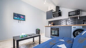 A compact living space with a bed, a small table, a TV, a microwave, a washing machine, and a compact kitchenette. - Charming studio near Roissy CDG (Vaujours)