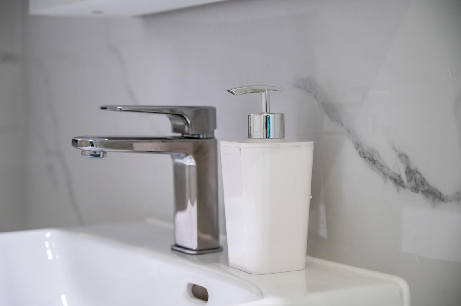 Een badkamer met een chromen kraan en een witte zeepdispenser op een witte wastafel.