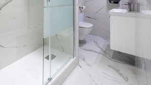 A modern bathroom with a glass-enclosed shower, a toilet, and a sink with a mirror. - Charming studio near Roissy CDG (Vaujours)