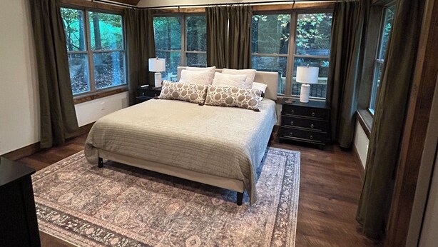 Un dormitorio con una cama grande, un ventilador de techo y vistas al exterior a través de amplias ventanas.