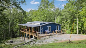Una cabaña azul con terraza, rodeada de bosque.