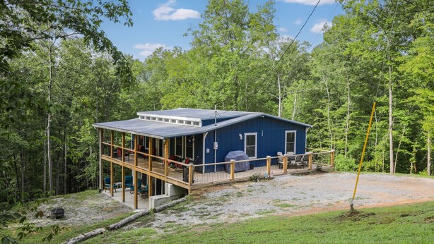 Una cabaña azul con terraza, rodeada de bosque.