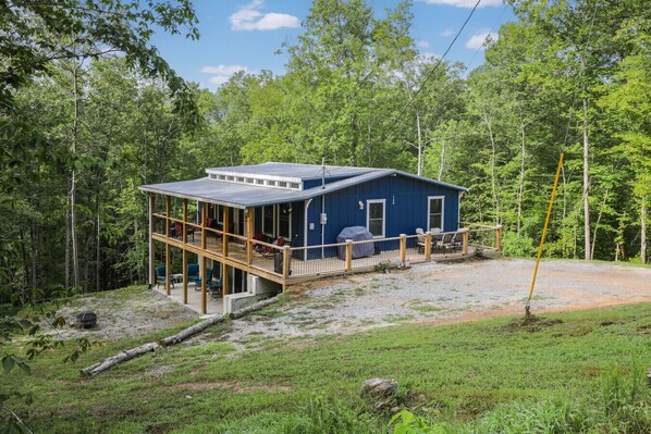 Una cabaña azul con terraza, rodeada de bosque.