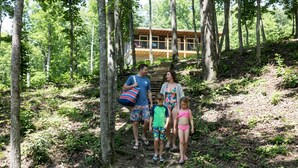 Una familia caminando por un sendero en el bosque, con una cabaña de madera al fondo.