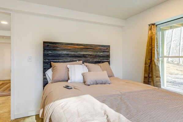 A bedroom with a large bed, a wooden headboard, and a window with curtains.