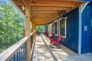 Une terrasse couverte avec un plancher en bois, des chaises rouges et une vue sur une forêt.