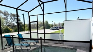A covered outdoor area with a pool, blue chairs, and a view of a parking lot.