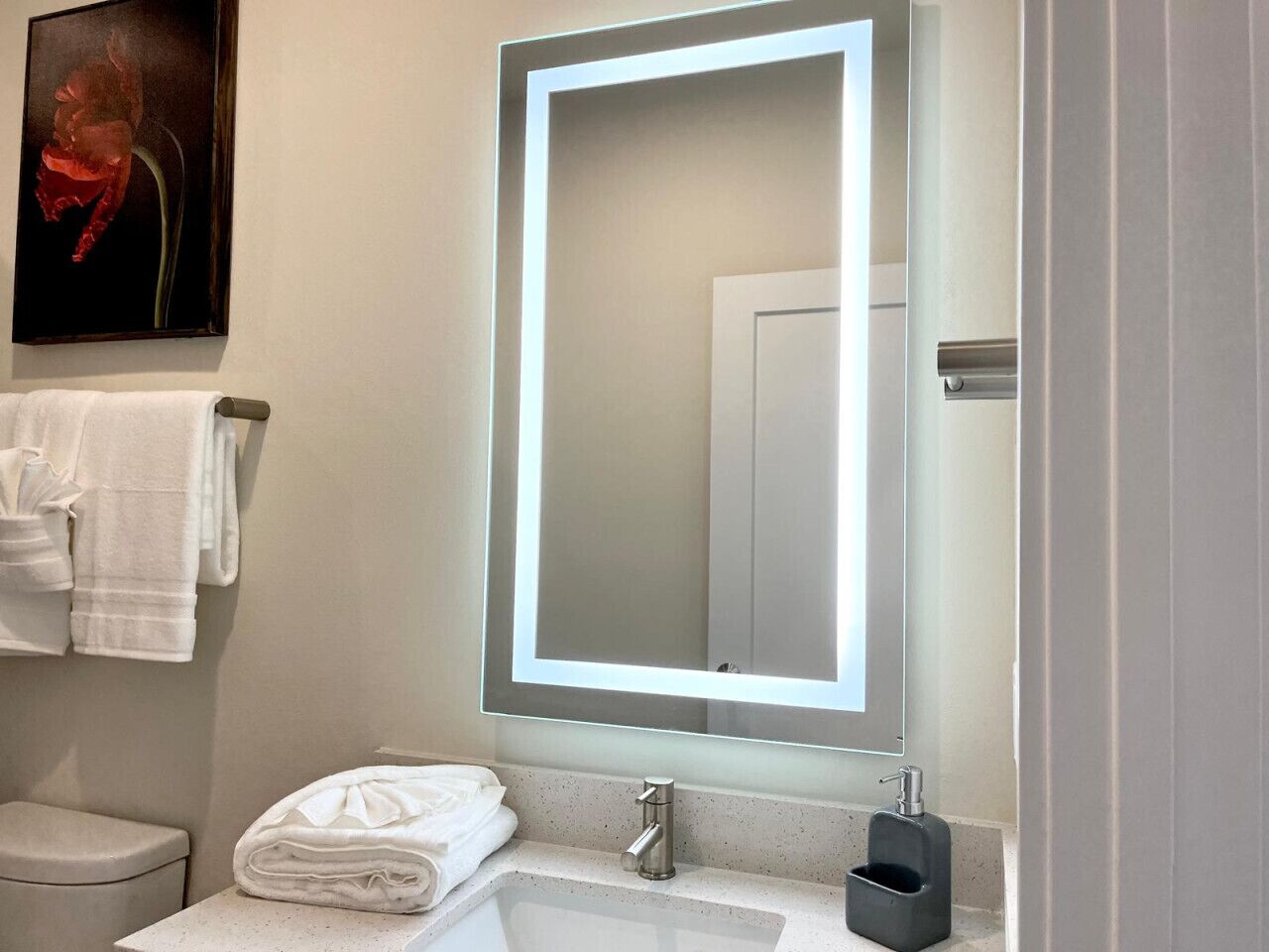 A bathroom with a white sink, a mirror with a lighted frame, and a toilet.