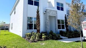 A modern two-story house with a white exterior, a stone accent wall, and a well-maintained front yard with grass and shrubs.