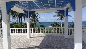 A covered outdoor area with a patterned floor, white railings, and a view of the ocean and palm trees. - We are directly on the beach with 50 meters of frontage and beautiful sunsets (Bobon)